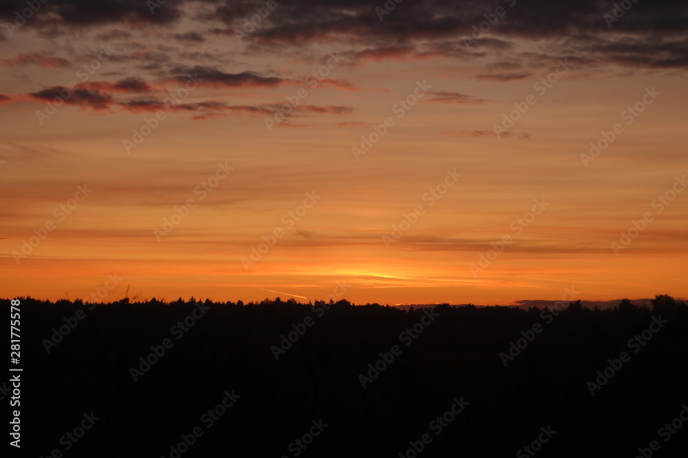 Sunset in orange hues over a dark strip of field and woods