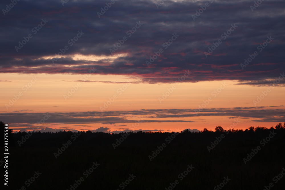 Sunset in summer in three distinct bands over field and woods