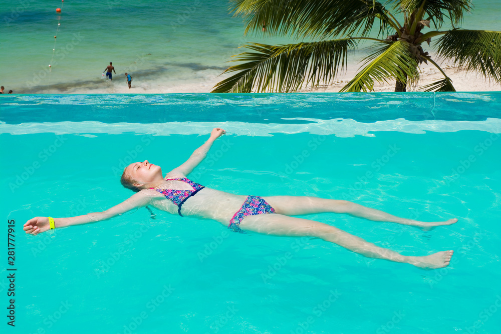 Caucasian teenager girl lying and relaxing in infinity swimming pool in luxury hotel, Punta Cana, Dominican Republic. Summer vacation concept
