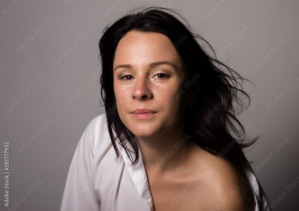 Fashionable woman in a mans white shirt with bare shoulder on a gray background Fashionable woman in a mans white shirt with bare shoulder on a gray background