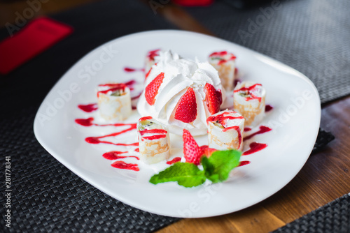 Dessert in a cafe. Dessert of cake with whipped cream, meringue, ice cream, decorated with fresh strawberries and mint. Rolls of dough with jam and cream.