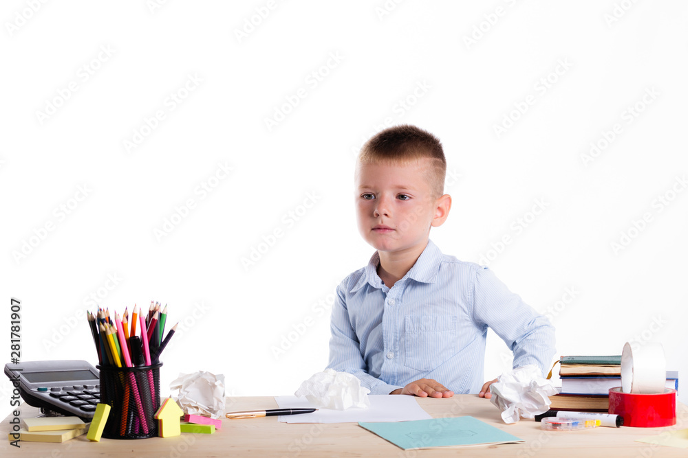 Cute little school boy with sad face sitting at his desk on white background.Unhappy intelligent children in shirt with blue eyes Cute little school boy with sad face sitting at his desk on white background.Unhappy intelligent children in shirt with blue eyes