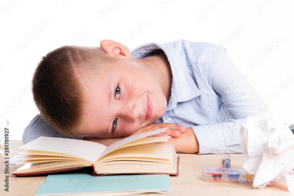 Cute little school boy with huge smile sitting at his desk on white background. Happy intelligent children in shirt with blue eyes, lies on table with book Cute little school boy with huge smile sitting at his desk on white background. Happy intelligent children in shirt with blue eyes, lies on table with book