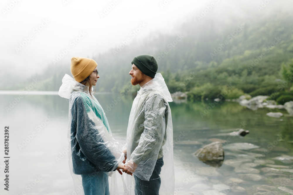 A couple in  rain coats in the rain. traveller couple standing on the lake shore and looking at the lake in rainy and foggy weather