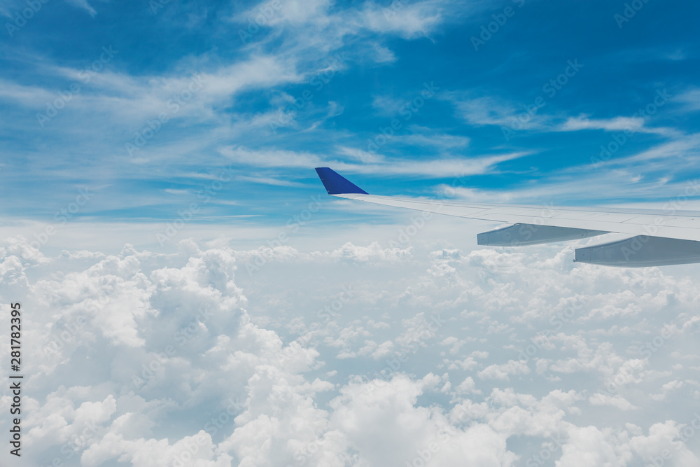 Fototapeta premium Airplane wing in cloudy bright blue sky, nice weather view from plane window seat.