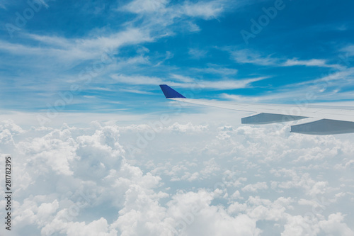 Airplane wing in cloudy bright blue sky, nice weather view from plane window seat.