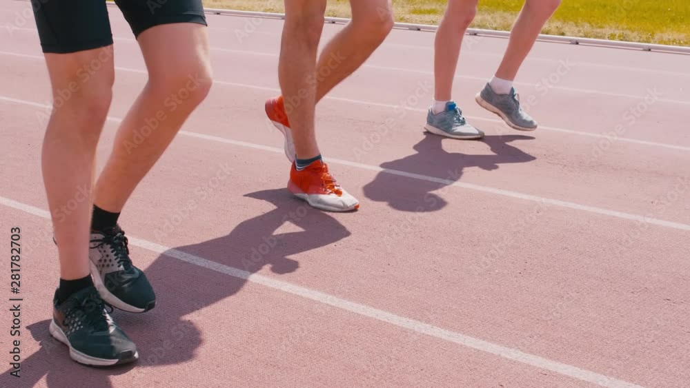 Low section shot of male sportsmen jogging to warm up legs through track on stadium Low section shot of male sportsmen jogging to warm up legs through track on stadium