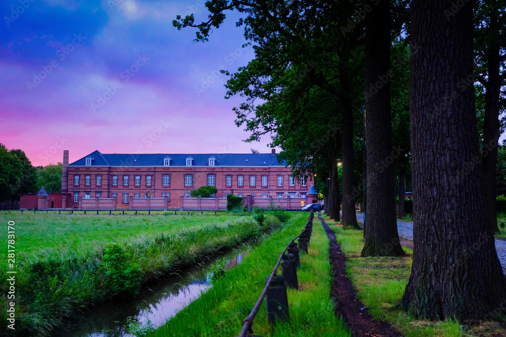 Vintage prison building in Hoogstraten, Belgium showing the tree lined road towards the main building under a sunrise sky