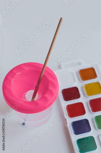 brush in a glass of water and a set of acrylic paints for drawing on a white background