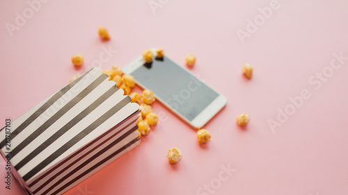 Movies and series by subscription, concept. smartphone lie next to a black and white papper striped box of popcorn
