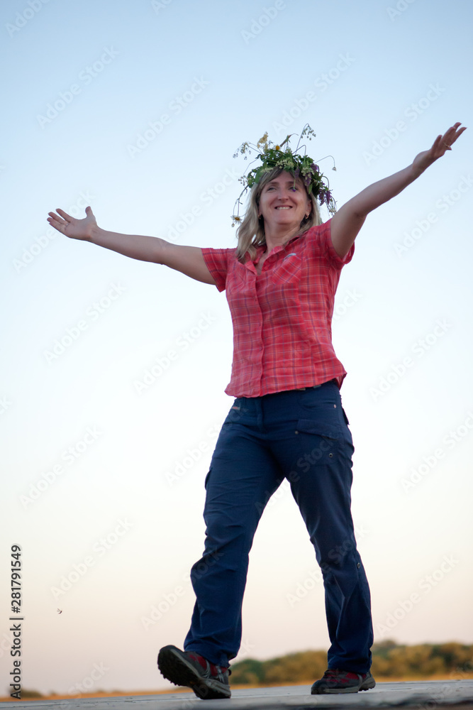 Full-length woman in a wreath of wild flowers in a red shirt walks on stage and a mosquito meets her