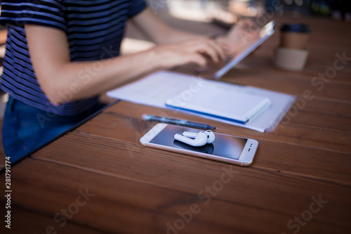 Feemale reelancer, with large wrist watch, works at a wooden table on tablet, with gadgets and papers. photo