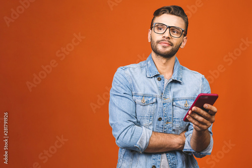 Great news! Happy young man in glasses typing sms isolated against orange background. © denis_vermenko
