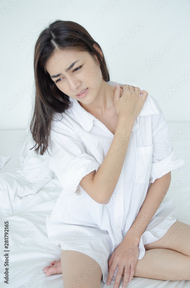 Asian women wear white pajamas in the bedroom. She has pain in the neck area. Asian women wear white pajamas in the bedroom. She has pain in the neck area.