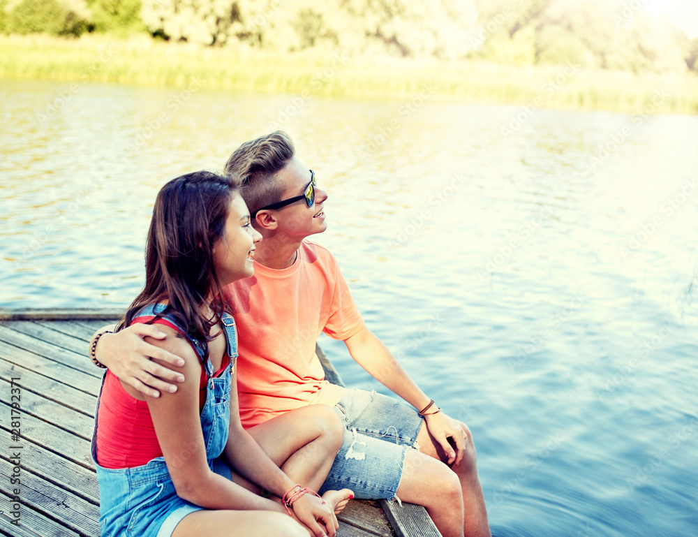 holidays, vacation, love and people concept - happy teenage couple hugging on river berth at summer