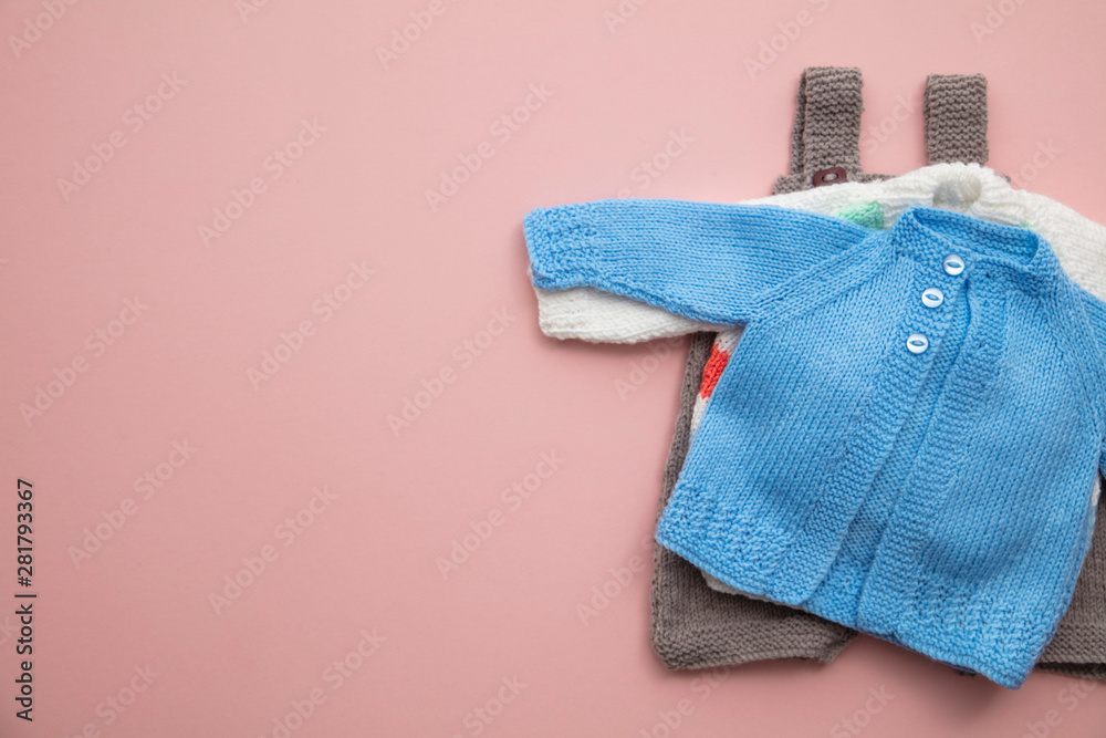 Cute knitted baby clothes layout on a pastel pink background