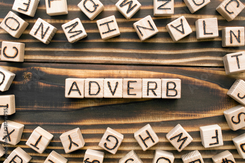 Adverb - word from wooden blocks with letters, describes or gives more information concept, random letters around, top view on wooden background photo