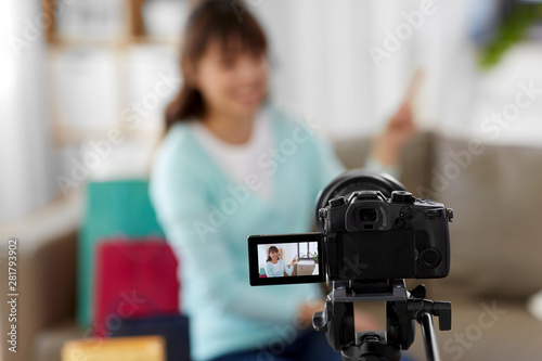 blogging, technology, videoblog and shopping concept - camera recording video blog of happy smiling asian woman or blogger pointing fingers upwards at home