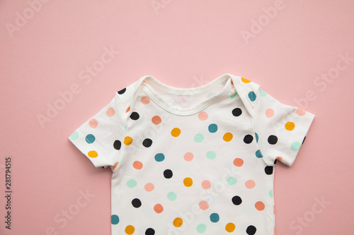 Cute polka dot baby body suit layout on a pastel pink background