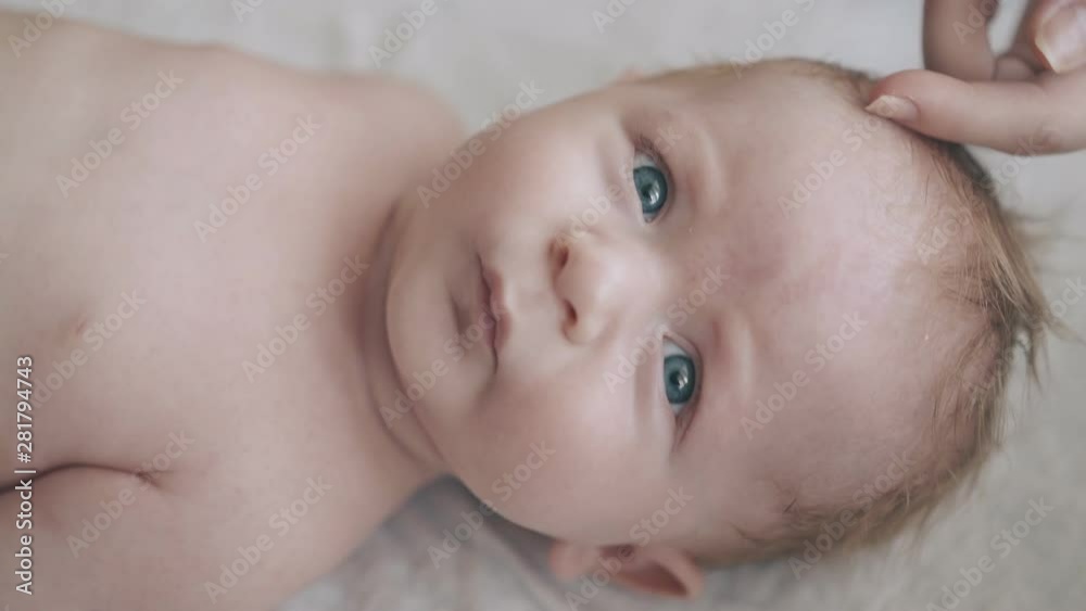 concentrated infant son with big blue eyes and fair hair lies on baby changing table looking at camera extreme closeup concentrated infant son with big blue eyes and fair hair lies on baby changing table looking at camera extreme closeup