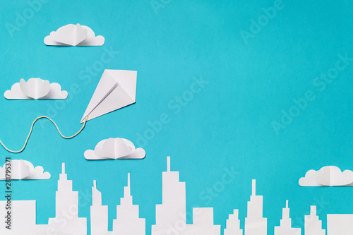 Fototapeta Naklejka Na Ścianę i Meble -  Origami kite in the sky with clouds and city silhouette paper cut banner design.