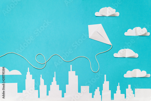 Origami kite flying trough paper cut clouds and a city silhouette. Paper cut banner template with copy space.