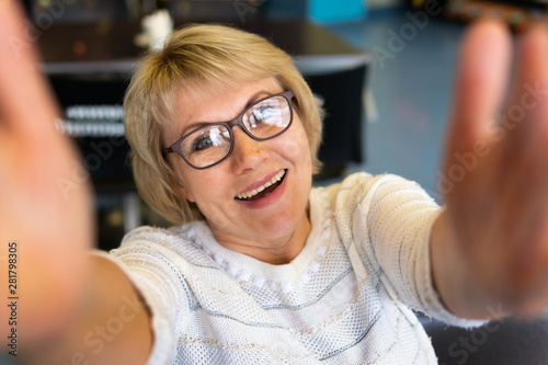 A middle-aged woman with glasses takes pictures of herself on the phone. She looks happy.