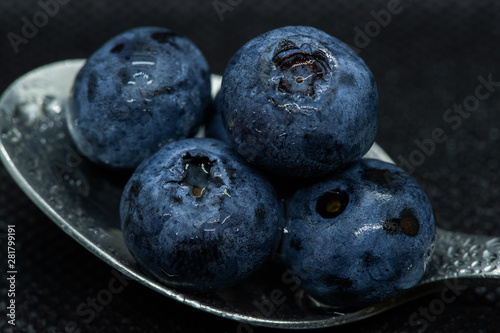 Blueberries Macro close-up photo of stacked and side by side in a teaspoon on a dark background covered with small drops of water.