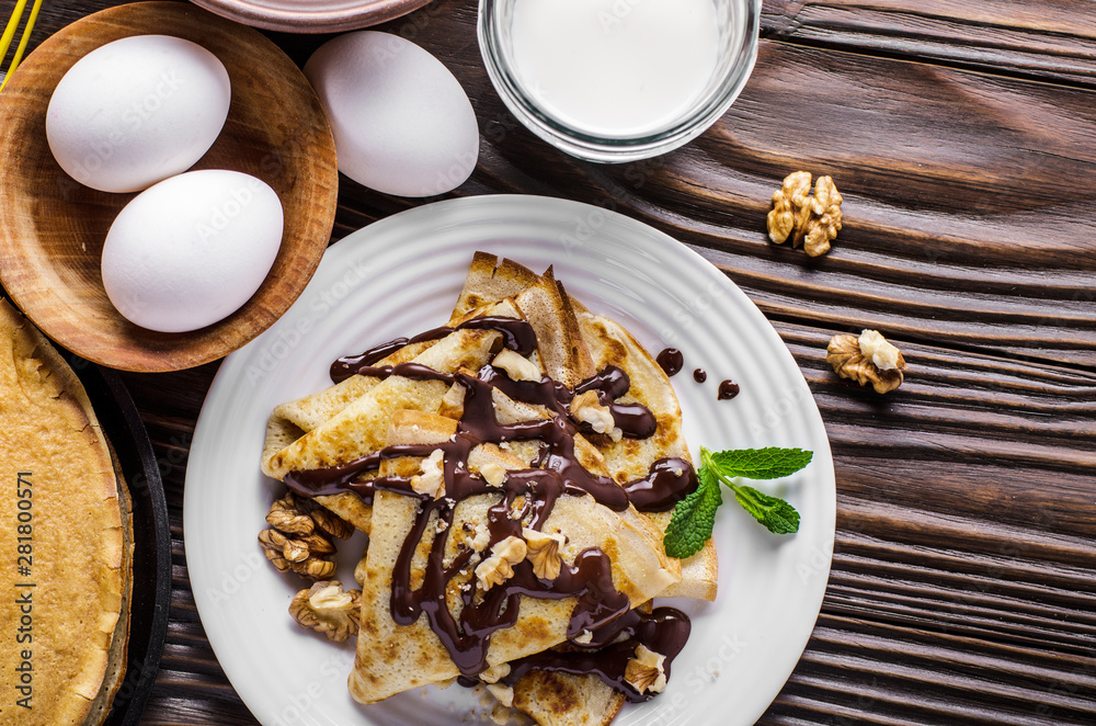 Flat lay French crepes with chocolate sauce walnuts eggs and flour on wooden kitchen table Flat lay French crepes with chocolate sauce walnuts eggs and flour on wooden kitchen table