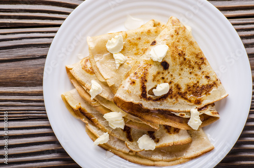 Flat lay of French crepes with butter and honey in ceramic dish on wooden kitchen table