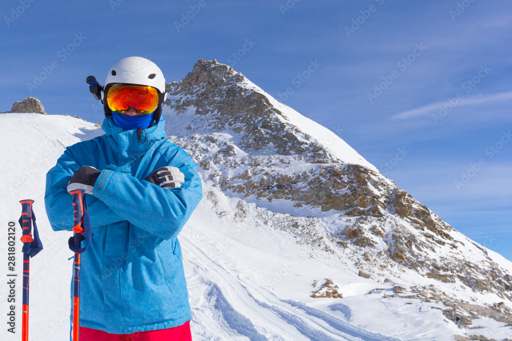Skier man with orange ski glasses in white helmet make photoshoot on top in Alps mountains. On the background of mountains. Close up view.