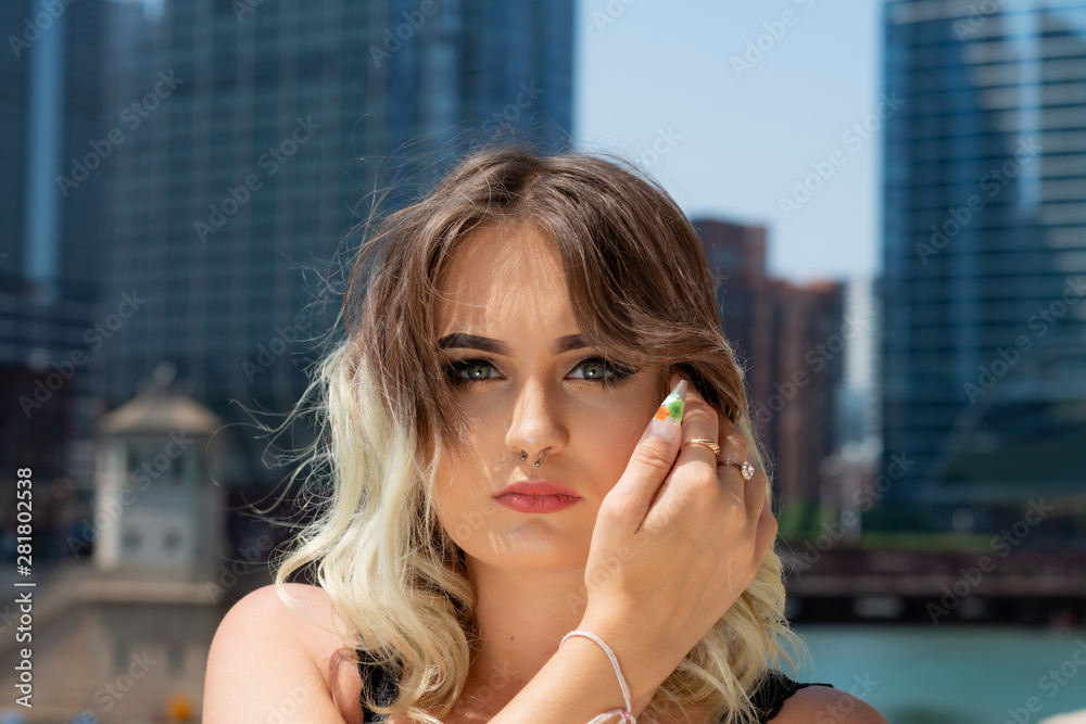 Fototapeta premium Beautiful Young Caucasian Girl with Barbell septum Nose Ring (Horseshoe Nose Ring) in Windy City at a sunny summer day.