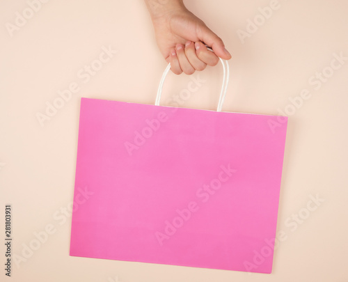 female hand holding a pink paper shopping bag