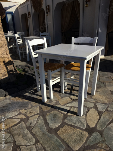 White-colored chairs and tables in typical Greek coffee. Outdoor cafe on a street of the typical Greek traditional village in Santorini, Firestefani, Greece.