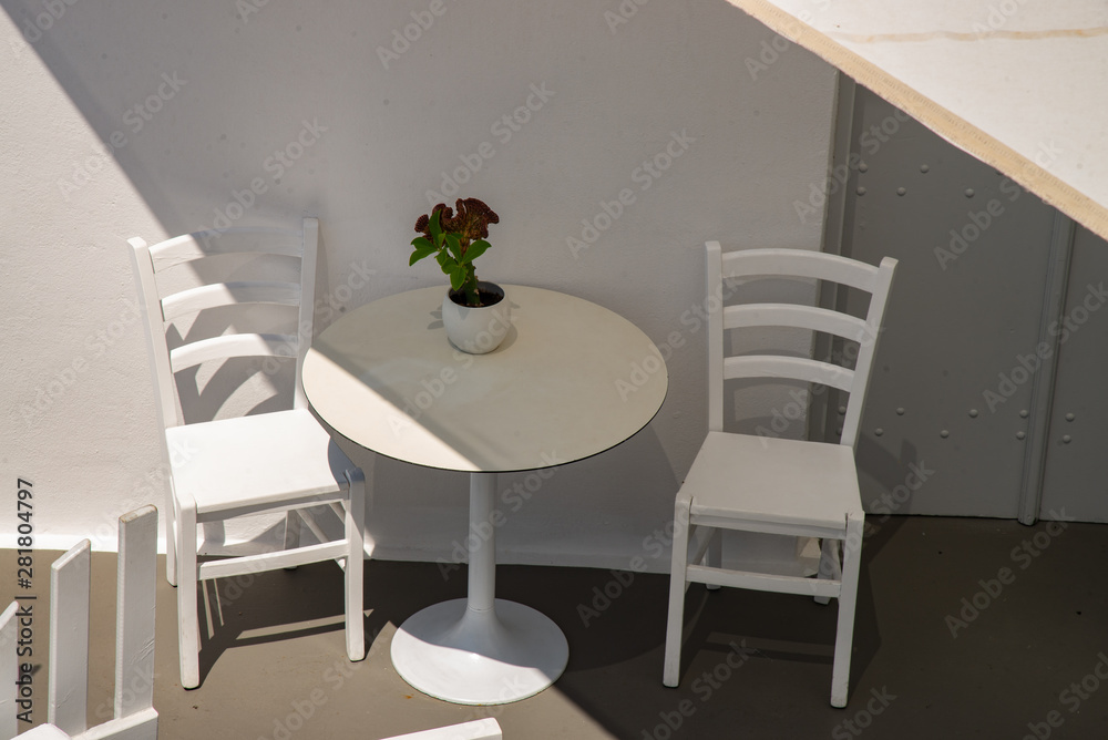 White chairs and tables with flowers on the typical Greek terrace. For breakfast or coffee break on the island of Santorini in Europe.