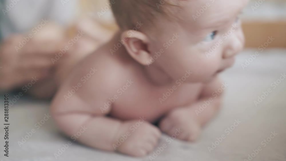 adorable newborn boy with large blue eyes and plump cheeks lies on stomach and enjoys back massage extreme close view adorable newborn boy with large blue eyes and plump cheeks lies on stomach and enjoys back massage extreme close view