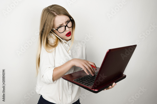 young beautiful business woman in eyeglasses working on laptop and speaking on smartphone simultaneously on the go isolated white background