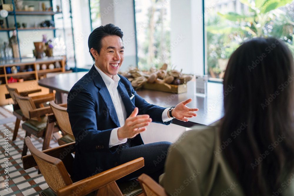 Φωτογραφία A young and attractive Chinese Asian man in a well-fitted navy suit and pocket square is talking to his companion in a meeting
