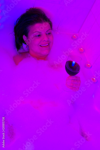 Lady takes a bubble bath with color light, candles and a glass of wine