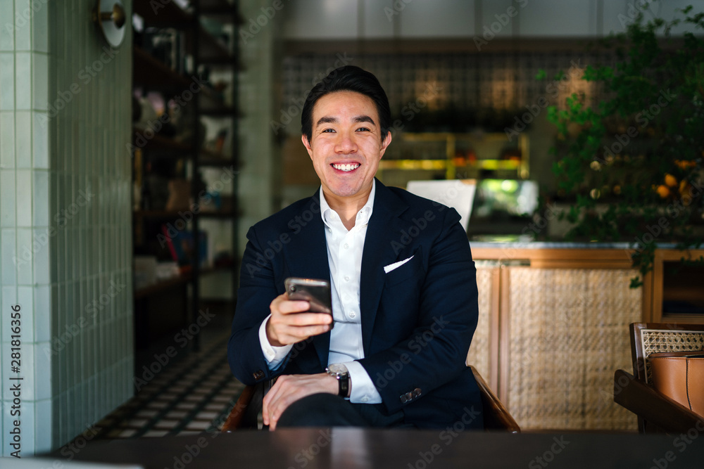 Φωτογραφία A young, handsome and successful Chinese Asian man smiles as he looks up from his smartphone