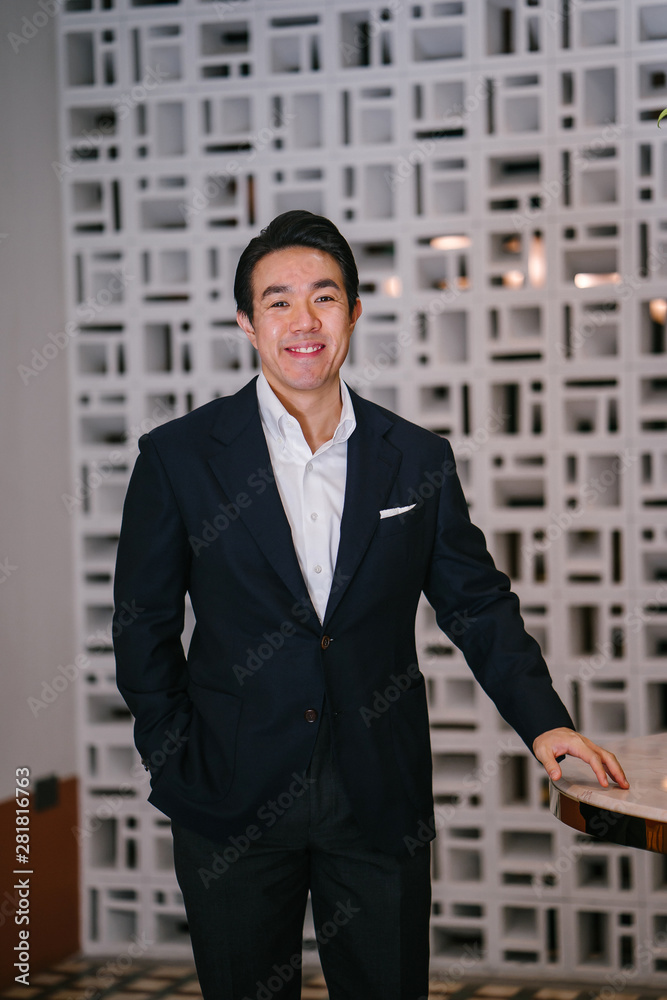 Portrait of a handsome, confident Chinese Asian businessman in a well-fitted navy blue suit and crisp white shirt and pocket square standing in his classy office. He projects success and confidence. Portrait of a handsome, confident Chinese Asian businessman in a well-fitted navy blue suit and crisp white shirt and pocket square standing in his classy office. He projects success and confidence.