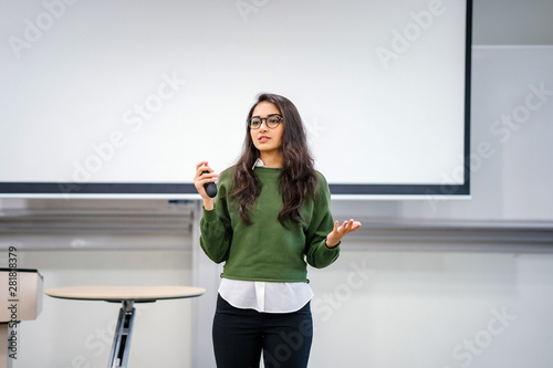 Photography Portrait of a young, beautiful, attractive and intelligent-looking Indian Asian woman wearing spectacles in a sweater giving a business presentation to an audience