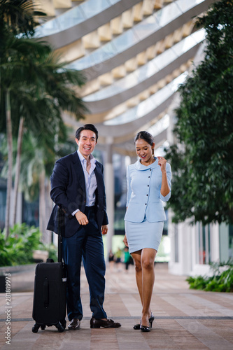 A handsome young Asian man in a suit is having a conversation with a professional woman in a blue suit. They are standing on the street in a modern city during the day. photo