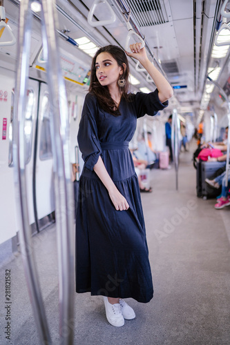  Portrait of a tall, slim, elegant and beautiful Indian Asian woman taking the train alone. She is holding by the handrails and watching the scenery go by. The train is modern and clean.