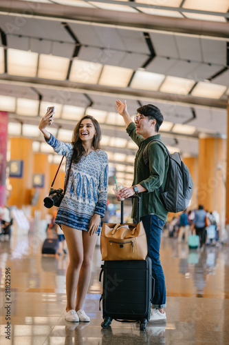 A young and diverse Asian couple (Korean man and his Indian girlfriend) take a selfie together in a new country. They have just arrived in a new country for a tour and are excited.