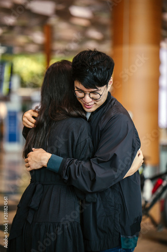 Portrait of a young and handsome Korean Asian man in a casual outfit and jacket hugging a woman at the airport. He looks sad that he is to be parted with his girlfriend.