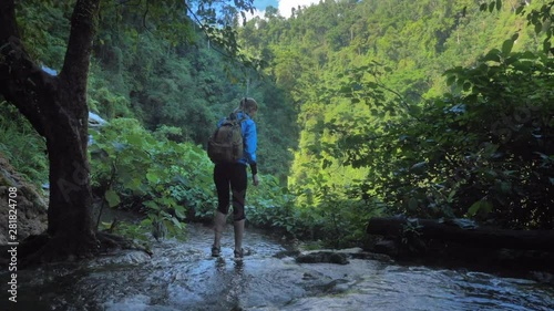 Woman walks through the waterfall Goa Tetes in Java island , looks around and raises her hands up, handled shot, No Color Grading photo