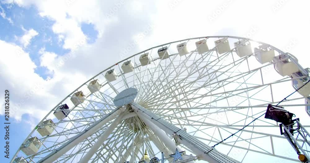 Ground up shot of a Ferris wheel on a warm summer day. Blue sky and clouds in the background. Ground up shot of a Ferris wheel on a warm summer day. Blue sky and clouds in the background.