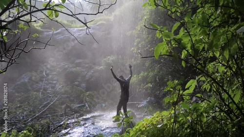 Slow motion wide shot of a happy African man dancing under a tropical waterfall shower. photo