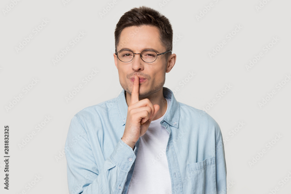 Headshot portrait man makes hush gesture pose over grey background Headshot portrait man makes hush gesture pose over grey background